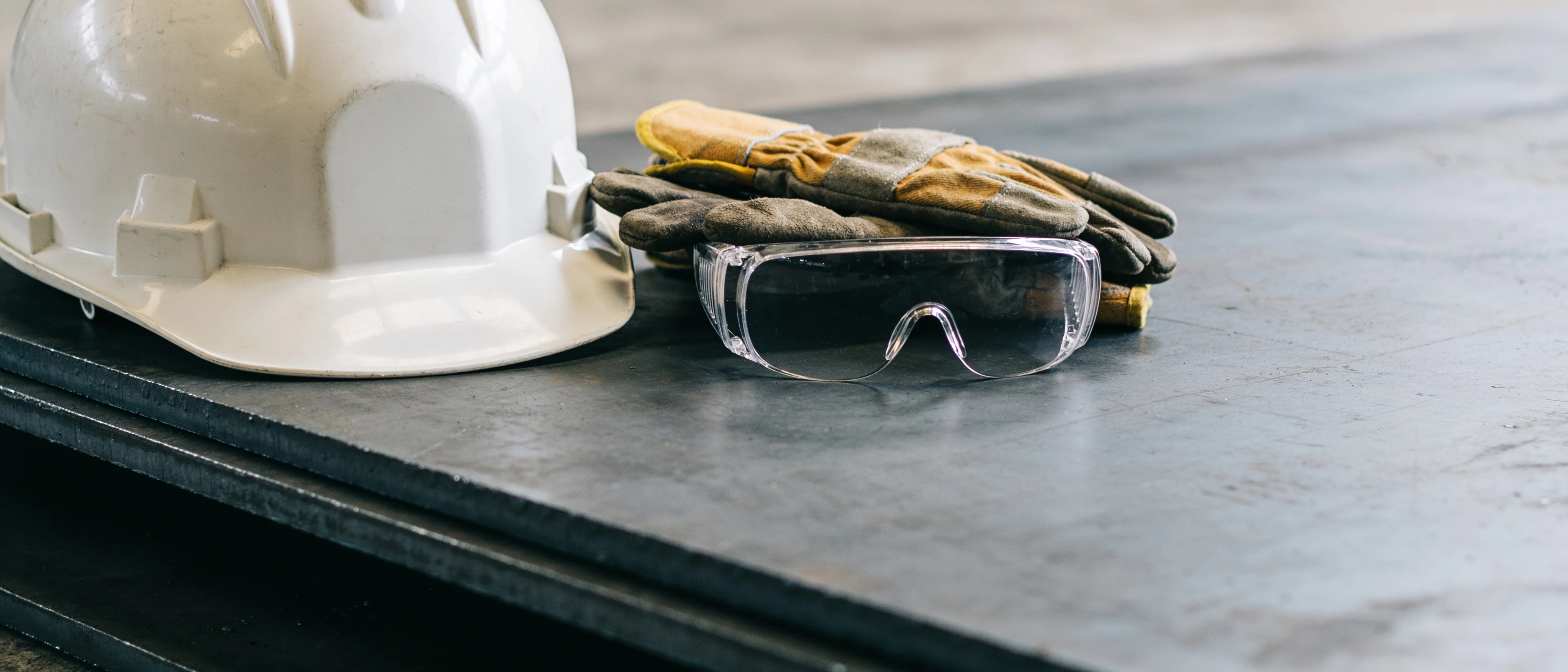 Schutzhelm, Arbeitshandschuhe und Schutzbrille liegen auf einem Stahlblech