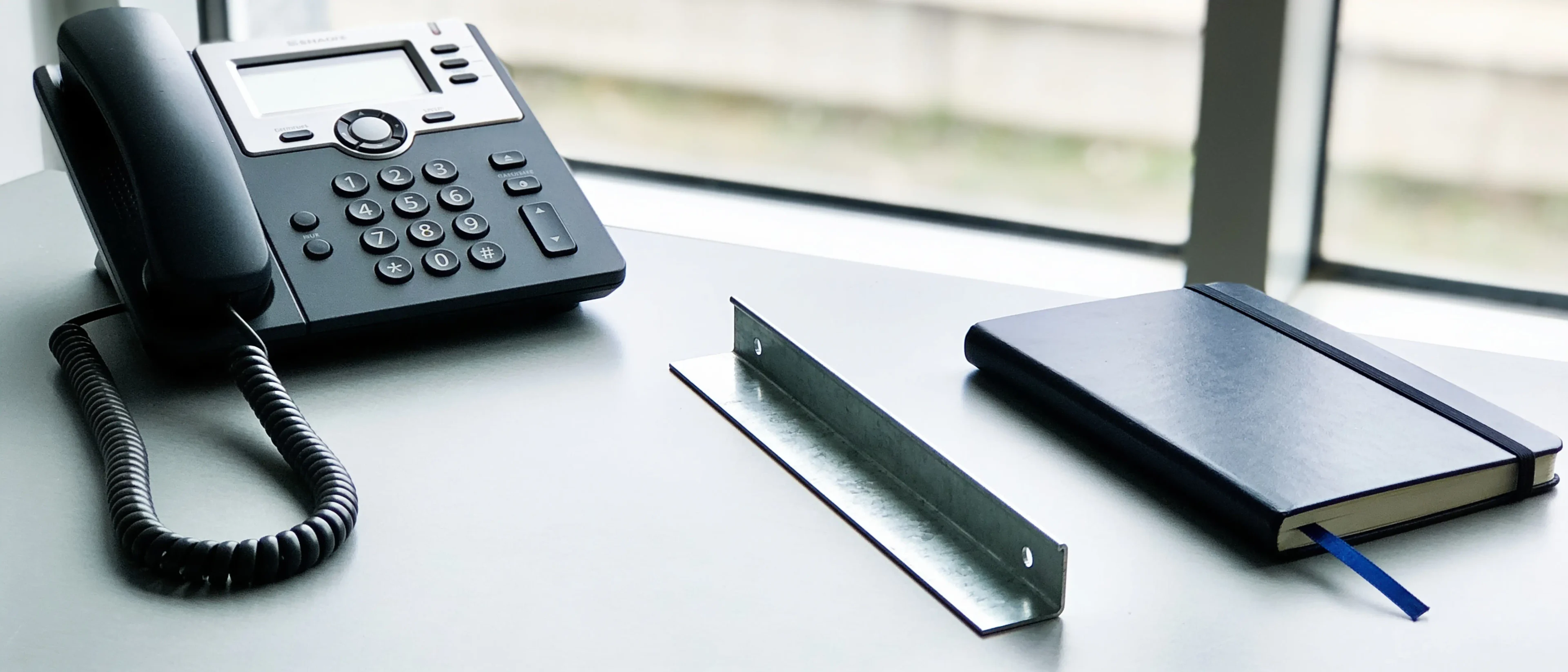 Telefon und Notizbuch auf dem Schreibtisch, daneben ein Profilabschnitt als Muster